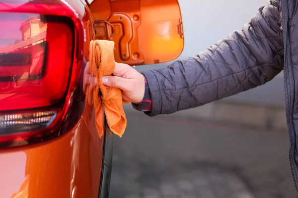 Homem depois de lavar limpa seu carro laranja com um pano na lavagem de carro. Mão masculina e carro corpo closeup . — Fotografia de Stock