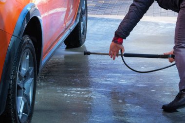 Self servis oto yıkamada su ile temizlik. Adam açık havada oto yıkama da onun turuncu araba yıkar.