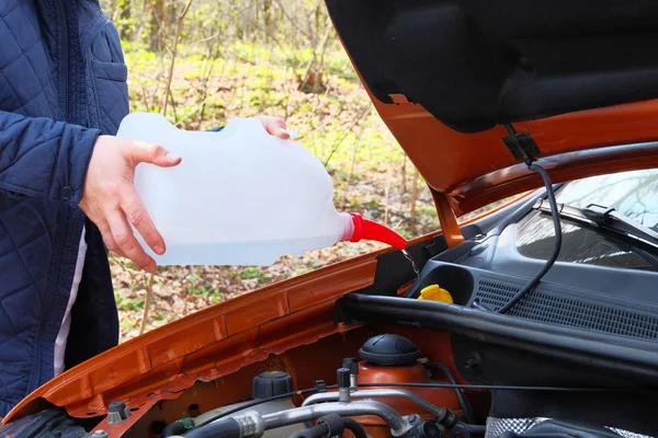 Car maintenance concept. Filling windshield washer fluid on car. Driver with washer fluid in his hands, close up.