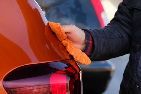 L'uomo dopo aver lavato pulisce la sua auto arancione con uno straccio all'autolavaggio. Maschio mano e corpo auto da vicino . — Foto Stock