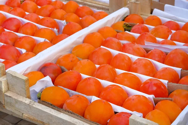 Biologische, oranje persimmon in houten kist worden verkocht op de lokale groenteboeren markt. Verkoop van vruchten na de oogst. Persimmons in greengrocery. — Stockfoto