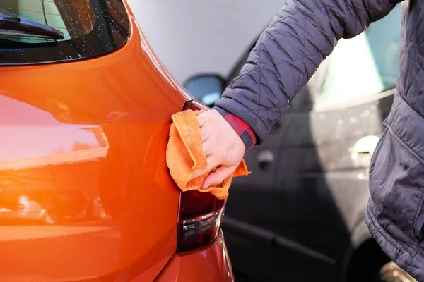 Man after cleaning wipes his orange car with a rag  at car wash. Male hand and car body closeup. — Stock Photo, Image