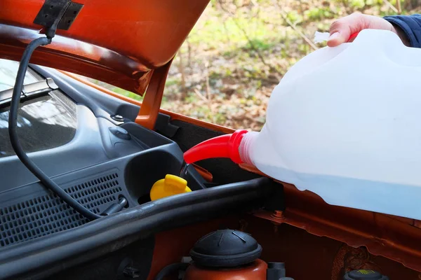 Filling windshield washer fluid in car. Driver with washer fluid in his hands, close up. Car maintenance concept.