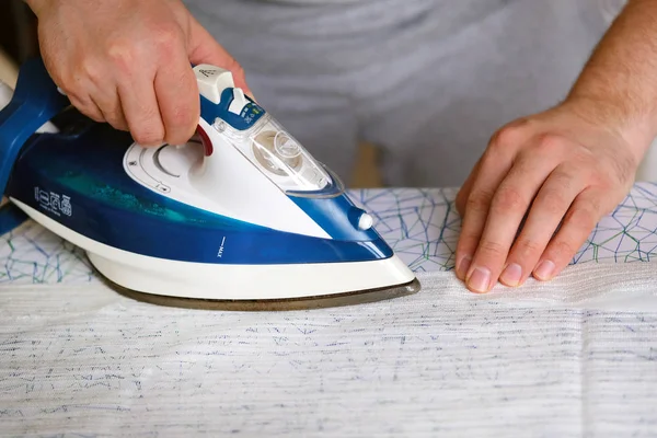 Hushållsarbete och hushållsbegrepp. Man är stryk textil på strykbräda hemma. Blått järn i man hand. — Stockfoto
