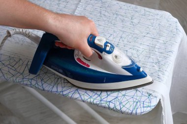 Ev işleri ve ev konsepti. Kocası evde giyim ütü yapıyor. Erkek eli giysiütüyor, yakından..