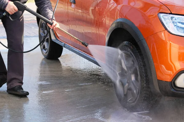 O homem lava o carro laranja na lavagem de carros. Limpeza com água na lavagem de carro self-service. Água ensaboada corre para baixo . — Fotografia de Stock