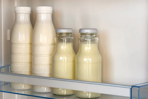 Dairy products in glass and plastic bottles on shelf of open empty fridge. White milk in refrigerator. Horizontal view.