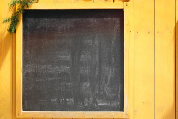 Empty space concept for advertising, mockup. Front view of a blank blackboard for text with Christmas tree branches and wooden surface in background.