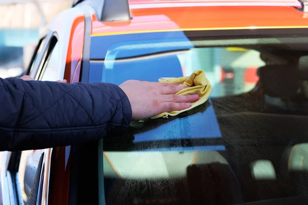 Man after washing wipes windshield of his orange car with a yellow rag at car wash. Close up of male hand and car window. — Stock Photo, Image