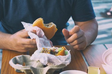 Kafede adam elinde Amerikan peynir burger. Bir restoranda yemek ve lezzetli fast food tadını çıkarın. Tonlu görüntü.