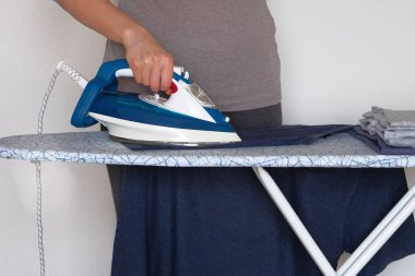 Evde giyim ütüleme. Genç kız evde giysiler ütüüyor. Kadın eli giysi ütüüyor, yakından..