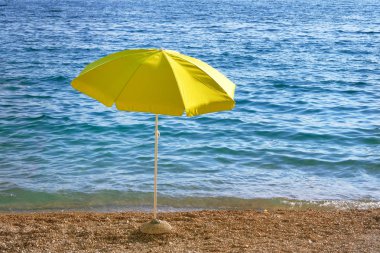 Yaz sahilinde sarı şemsiye. Güneş şemsiyesi ile deniz plajı turistleri bekliyor. Mutlu yaz tatilleri kavramı.