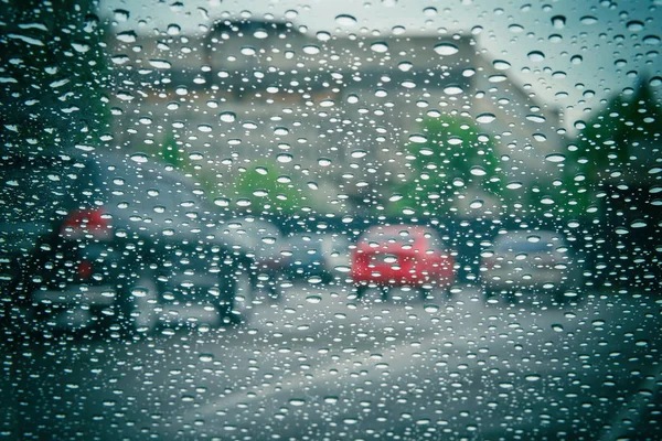 Road view through car window with rain drops. Car window on a rainy day. Highway view, background is out of focus.