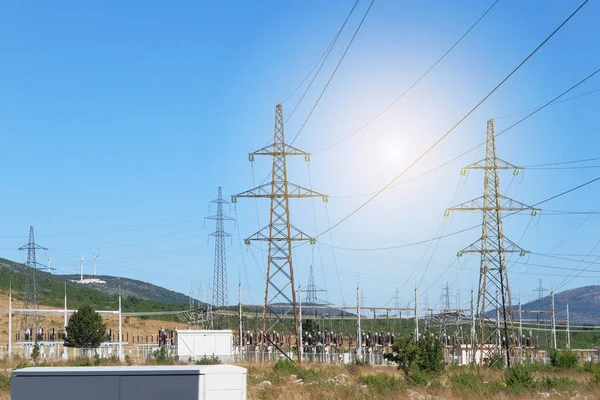 Elektrické vysílání pylonů proti modré obloze. Vysokonapěťové elektrické tyče s větrnými turbínami. — Stock fotografie