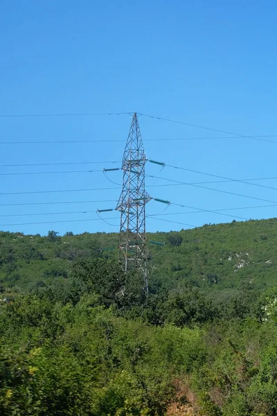 Vysokonapěťové elektrické tyče v horách. Elektrický přenos pylonů proti modrému nebi. — Stock fotografie