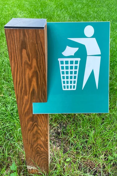 Sign of throw the trash in the trash can on background of green grass in park. Symbol on metallic plate.