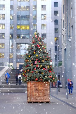 Parlak toplar ve oyuncaklarla süslenmiş Noel ağacı ofis merkezinin girişinin önünde duruyor. Şehirde kar yağıyor..