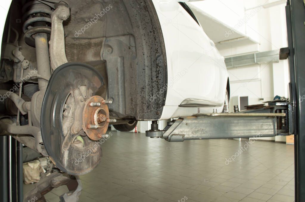 Front suspension of a white car mounted on a lift in a car repair shop