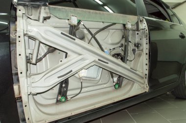 Koyu gri bir arabanın sol ön kapısına, dış paneli sökülmüş elektrikli cam kaldırıcının mekanizması.