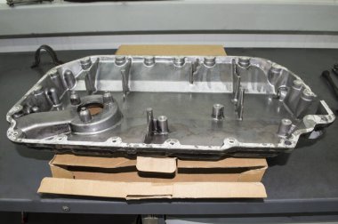 İçten yanmalı motorun alüminyum yağ tabakası gri metal bir masanın üzerindeki karton kutunun üzerinde kusurlu duruyor.