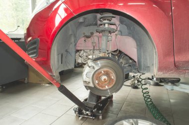 Bir oto tamirhanesinde sol ön tekerleği sökülmüş kırmızı bir arabaya monte edilmiş, motor bir Jack 'in üzerinde.