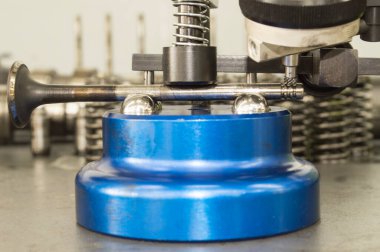 Bir araba tamirhanesinde mavi bir aletle valf sapının bükülmesini kontrol etmek için uygulanan prosedürün yan görüntüsü