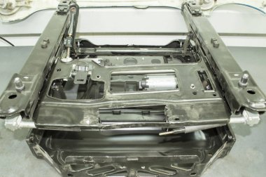 Siyah metalden yapılmış arabanın ön koltuğunun iskeleti araba tamirhanesinde gri bir masanın üzerinde duruyor.