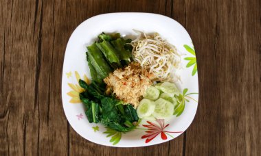 Sayur urap ahşap arka plan üzerinde. Baharatlı rendelenmiş hindistan cevizi ile pişmiş sebze. Endonezya geleneksel gıda.