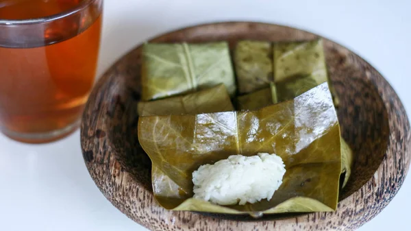 Fermented sticky (tape ketan) wrapped in guava leaves and a glass of tea on white background.