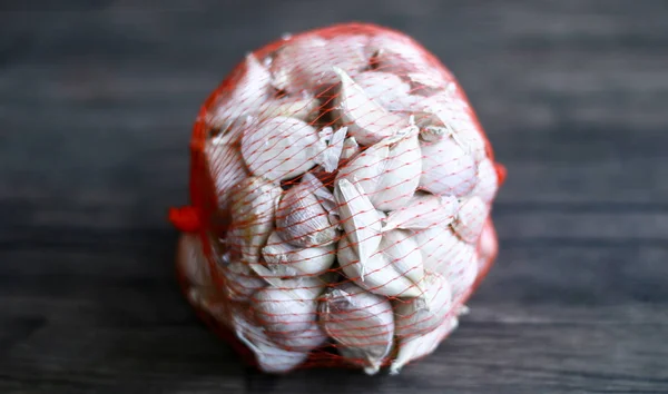 Garlic in a mesh bag on wood background.
