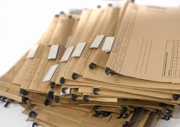 Stack of multiple brown marked paper documents with plastic clips sitting on top of plain white surface
