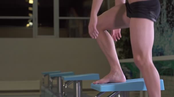 Пловец поднимается на скамейку перед прыжком в бассейн — стоковое видео
