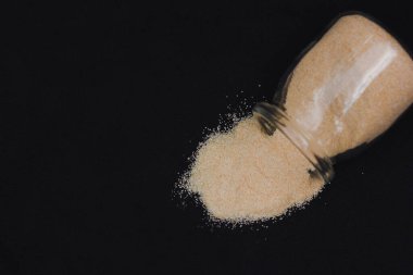 Gün ışığında siyah bir yüzeyde cam bir kavanozdan şeker dökülür.