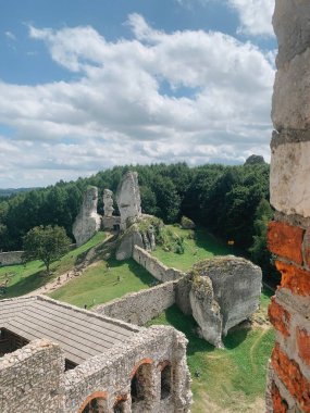 Tarihi bir bölgede bulutlu bir gökyüzü altında antik kaya oluşumları ve yemyeşil yemyeşil manzaralar.