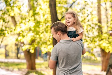  Baba ve küçük kızı sokakta parkta oynuyorlar, bir bebek babasının omuzlarında oturuyor, yakın plan, çocuk gülüyor, konsept mutlu babalar günü. Kaliteli fotoğraf