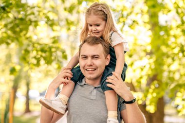  Baba ve küçük kızı sokakta parkta oynuyorlar, bir bebek babasının omuzlarında oturuyor, yakın plan, çocuk gülüyor, konsept mutlu babalar günü. Kaliteli fotoğraf
