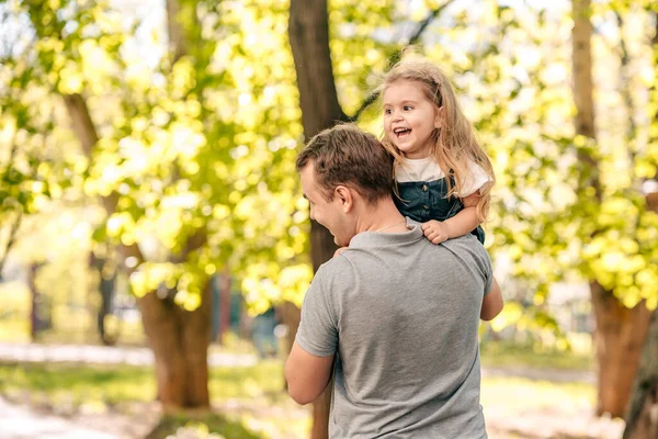  Baba ve küçük kızı sokakta parkta oynuyorlar, bir bebek babasının omuzlarında oturuyor, yakın plan, çocuk gülüyor, konsept mutlu babalar günü. Kaliteli fotoğraf