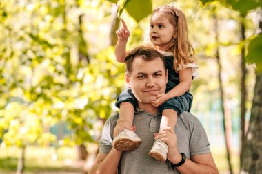  Baba ve küçük kız sokakta parkta oynuyorlar, bir bebek babasının omuzlarında oturuyor, yakın plan, mutlu babalar günü konsepti. Kaliteli fotoğraf