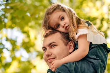  Baba ve küçük kızı sokakta parkta oynuyorlar, bir bebek babasının omuzlarında oturuyor, çocuk babaya sarılıyor, yakın plan, mutlu babalar günü konsepti. Kaliteli fotoğraf