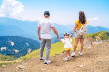 Çocuklu mutlu bir aile dağın zirvesinde güzel manzaraya bakıyor. Dağlarda yaz gezisi, seyahat konsepti