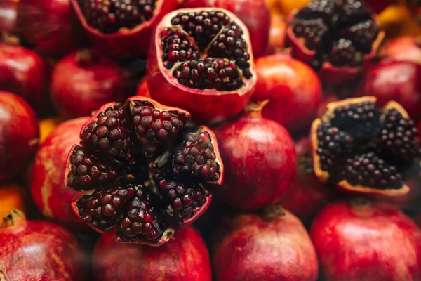 Sappige en rijpe granaatappel met schil verwijderd, blootleggen van verse zaden, leggen op stapel granaatappels — Stockfoto