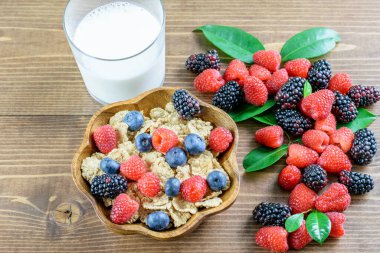 Mısır gevreği integrali, böğürtlen çeşitleri ve ahşap arka planda bir bardak süt. Sağlıklı beslenme, dengeli meyve diyeti kavramı. 