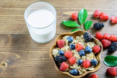 Mısır gevreği integrali, böğürtlen çeşitleri ve ahşap arka planda bir bardak süt. Sağlıklı beslenme, dengeli meyve diyeti kavramı.