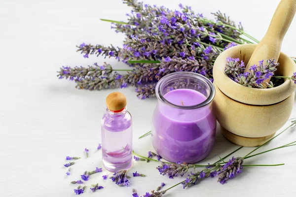 Lavender body skin oil, candle and lavender flowers on the white background. Aromatherapy and skin care concept.