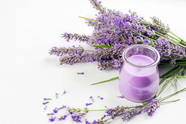 Violet lavender flowers and lavender aromatic candle in the glass jar on the white background.