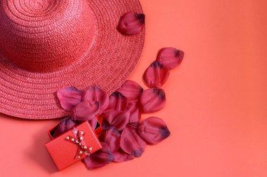 Kırmızı hasır şapka ve kırmızı arka planda gül desenli kırmızı hediye kutusu. Tek renkli fotoğraf, düz yatak, metin için boşluk. 