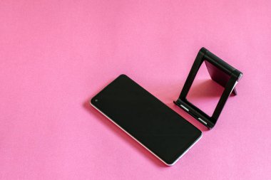 Akıllı telefonlu düz bir fotoğraf, pembe arka planda telefon standı. Modern teknoloji kavramı. 