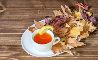 Beyaz çay tabağında limon olan bir fincan meyve çayı. Mevsimin sembolü olarak kuru renkli yapraklar, rahatlama ve yaşam tarzı. 