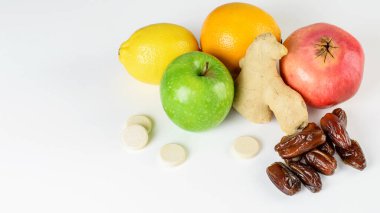 Beyaz arka planda tropikal narenciye, zencefil, hurma meyvesi ve multivitamin haplarından oluşan bir grup. Ev yapımı antivirüs ilacı, bağışıklık sisteminin destekçisi.. 
