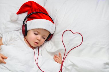 Bir şirin yürümeye başlayan çocuk santa şapka ve kırmızı Kulaklığımda uyuyor